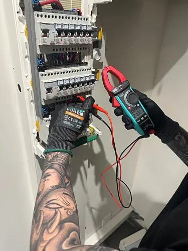 Technicien AUREA ganté mesurant un tableau électrique à la pince ampèremétrique